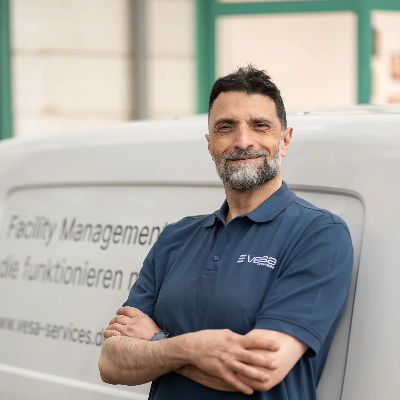 Mann mit verschränkten Armen und blauem Polohemd lehnt an einem weißen Transporter mit Vesa Services Logo.