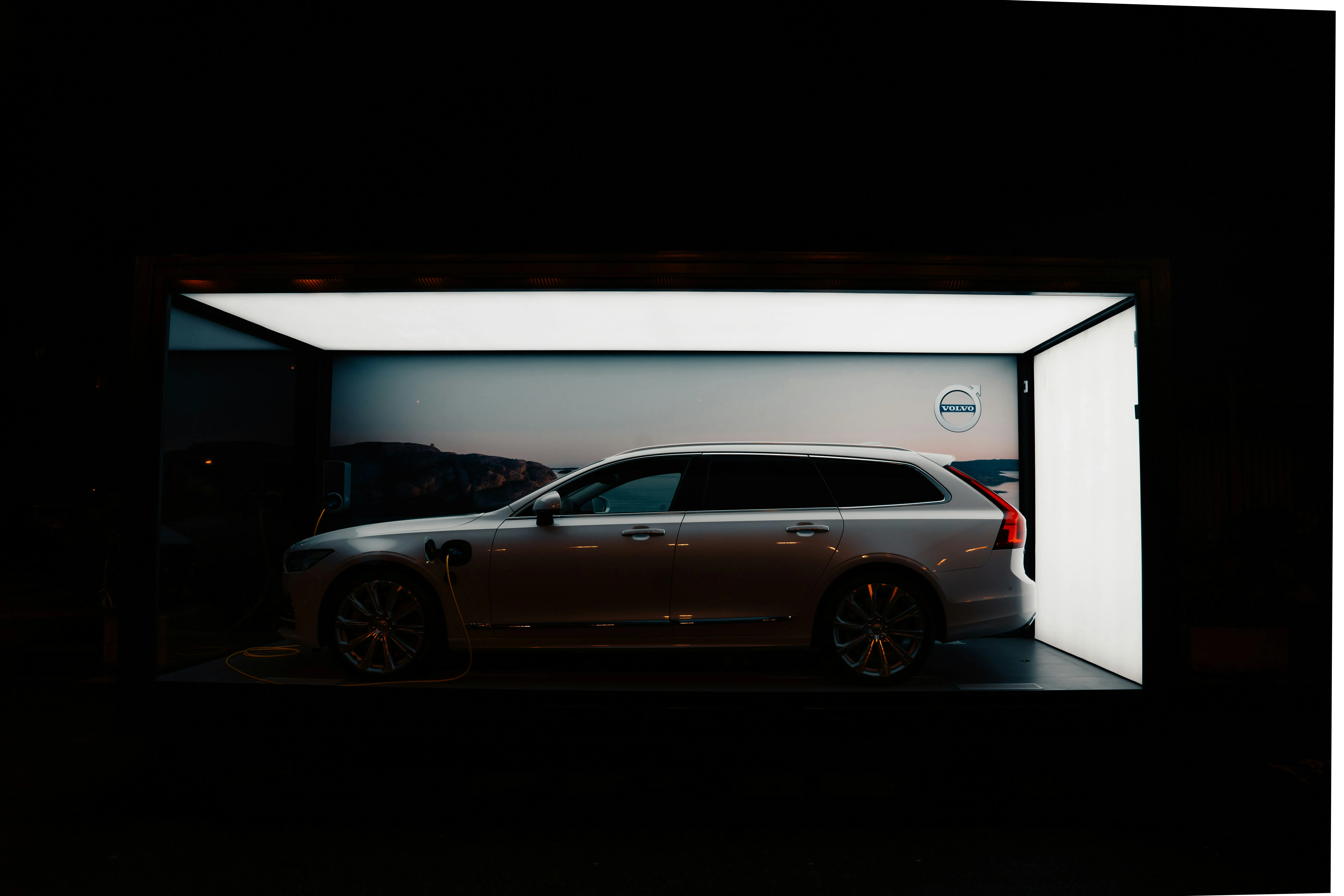 Ein silberner Volvo Kombi lädt in einem beleuchteten Ausstellungsraum bei Nacht.